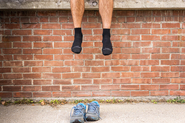 Legs hanging over a wall with feet in black socks, shoes waiting patiently below