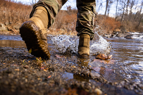 Feet wearing military combat boots walking through a stream