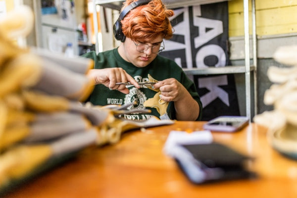 Young employee carefully cutting leather bits from sewed glove