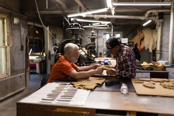 An older employee teaching a new employee how to inspect the leather
