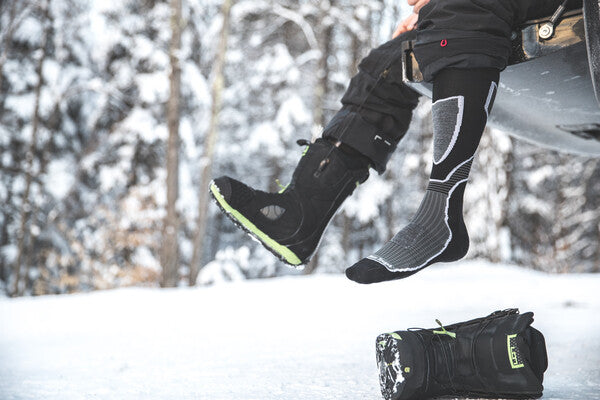 Snowboarder outside pulling on snowboard boots over his socks