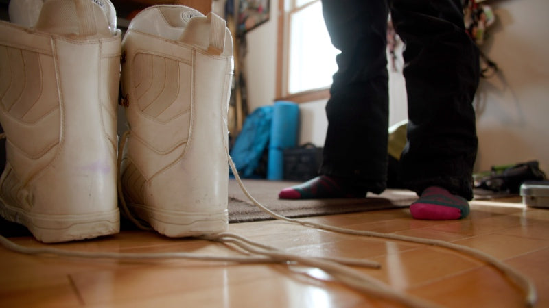 Feet in Darn Tough socks standing next to snowboard boots