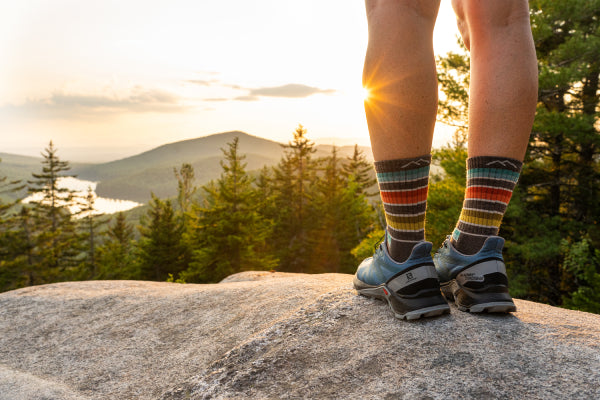 Hiker in the Darn Tough Decade Stripe Micro Crew Socks at the summit of a mountain looking at the sun over another mountain