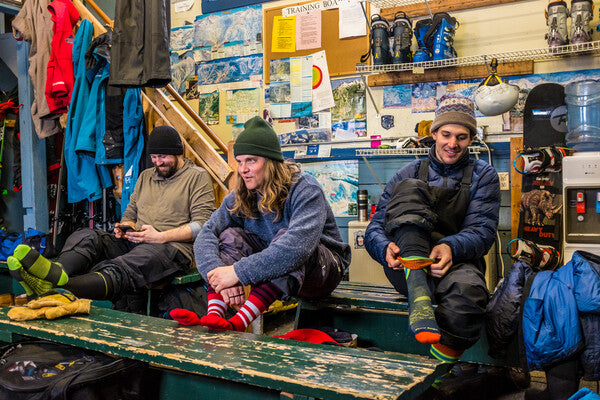 A group of riders seated in the lodge with their boots off