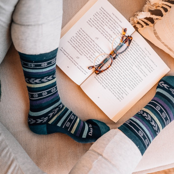 Person seated on bed looking very cozy with a book and darn tough's comfortable socks