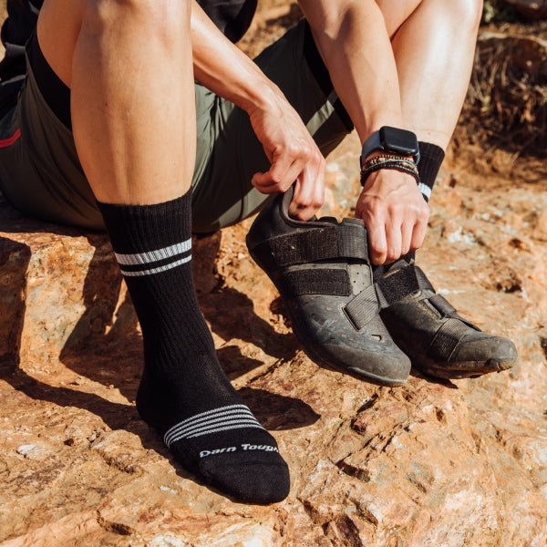 Mountain biker pulling on mountain bike shoes over close-fitting darn tough socks