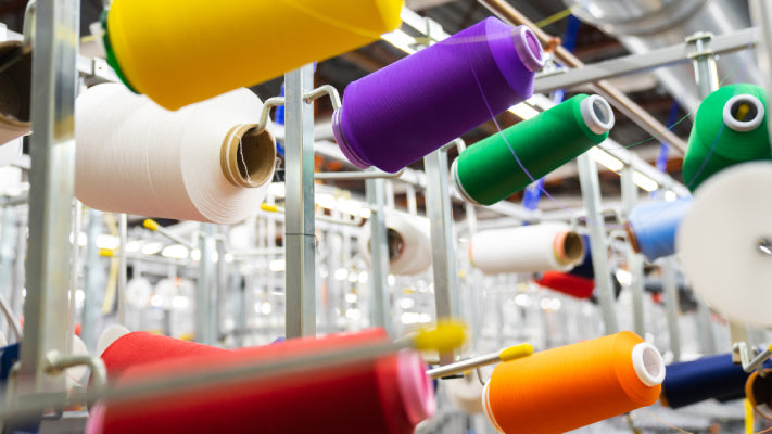 A row of yarn cones in the Mill in bright, bold colors including green, yellow, red, and purple