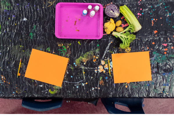 Art supplies for food stamping laid out on the table, including paper, paints, and vegetables