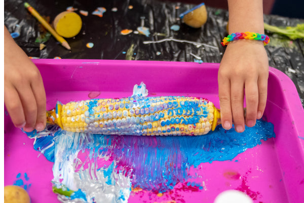 Child rolling corn cob in paint