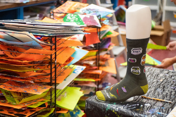 Preserve knit to give sock next to drying stacks of artwork