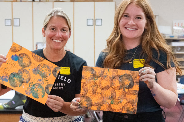 Alex and Michelle holding up some of the artwork from the art class for knit to give