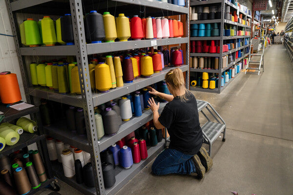 A worker kneeling by a shelf of merino wool yarns to pick the right ones