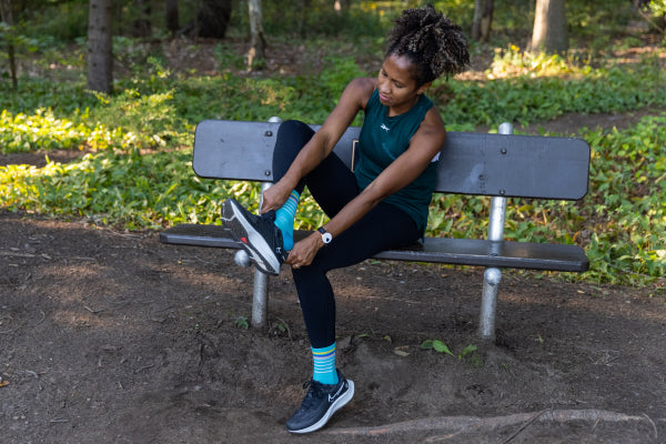 Runner seated on bench adjusting their shoes wearing blue run socks