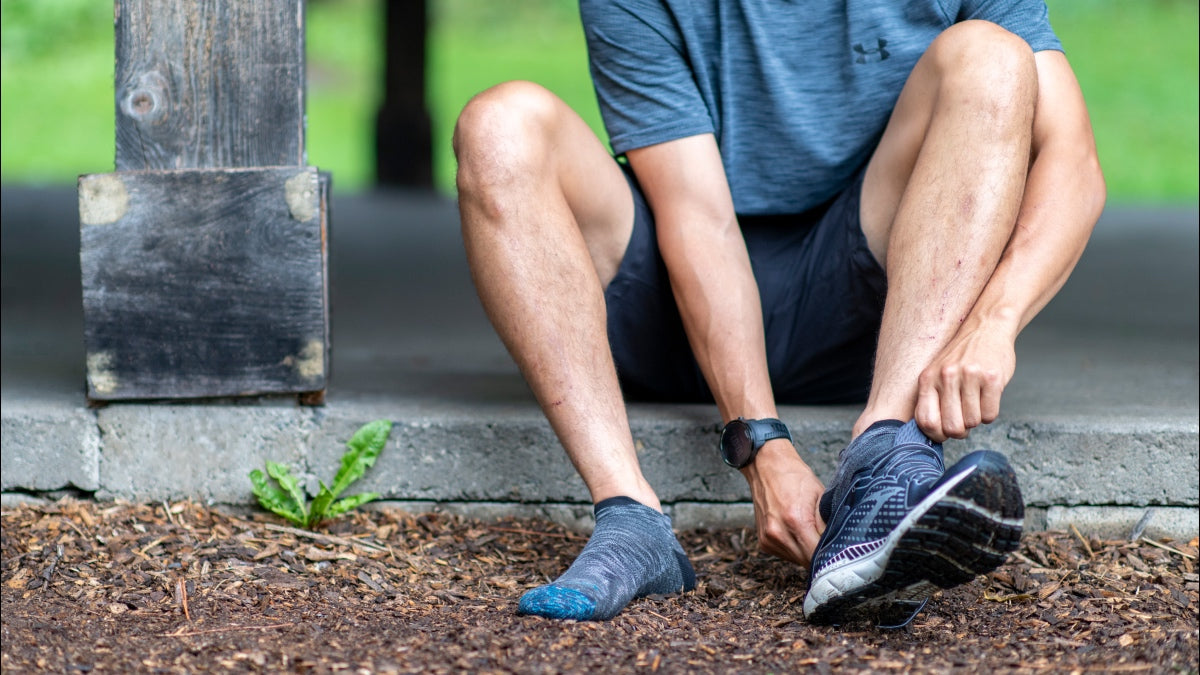 Person seated ground wearing no show running socks and putting on running shoes