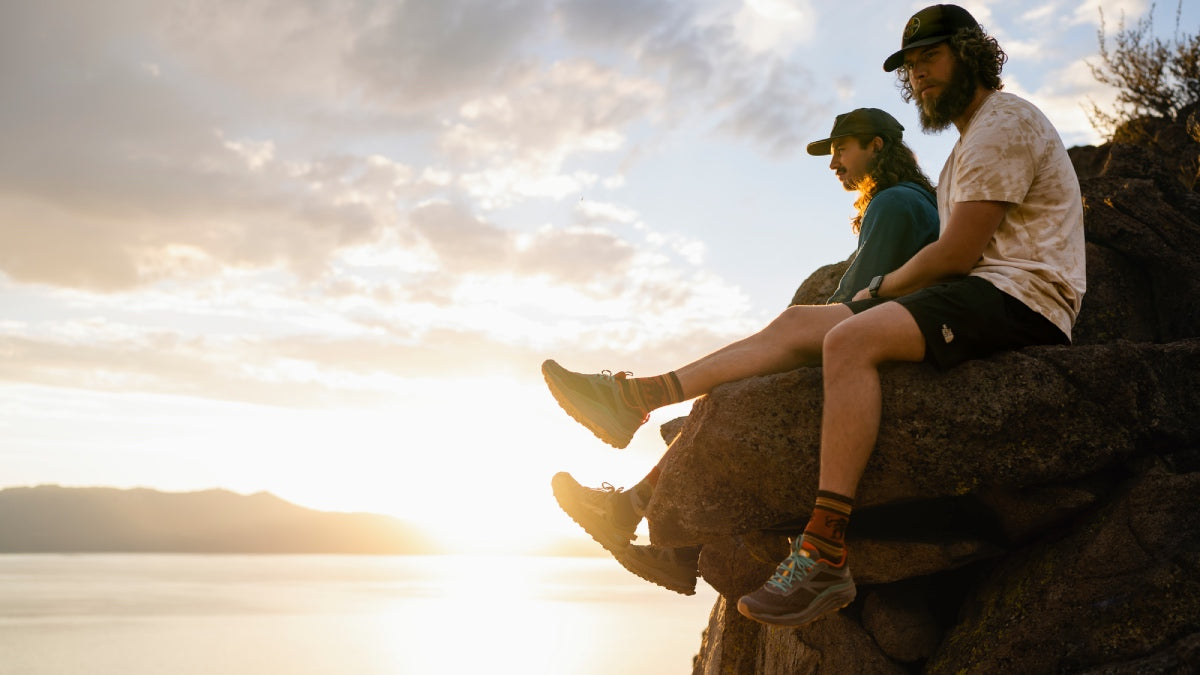 Two guys seated on a rock ledge watching the sunset wearing the best men's hiking socks