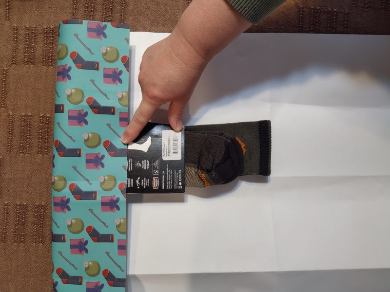 Person folding loose edge of paper over socks to see if it's enough wrapping paper