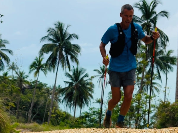 Kris training, holding trekking poles, palm trees behind him