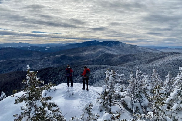 Two hikers standing on a summit in winter with beautiful snow-covered trees and mountains