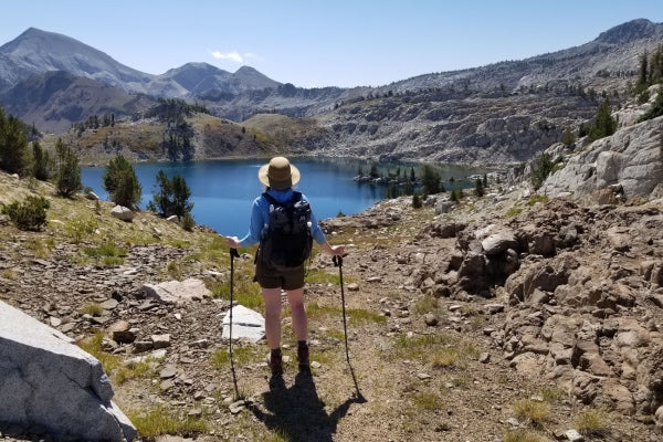 A hiker in a sun hat and shorts looking out at a lake while summer hiking