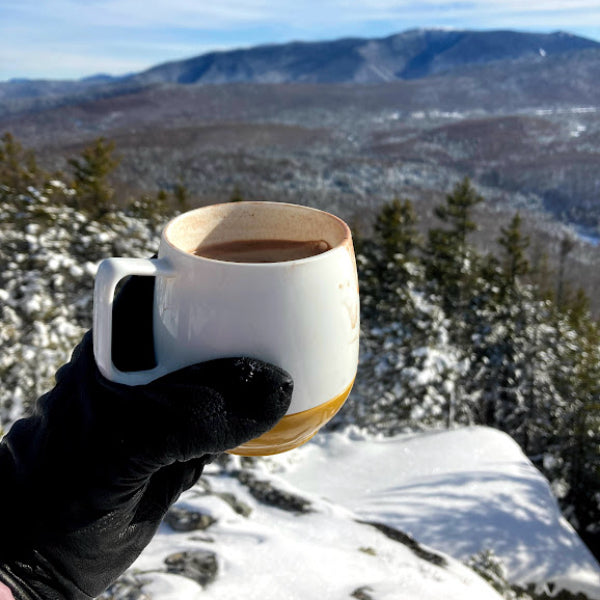Gloved hand holding cup of hot cocoa on summit of mountain in winter