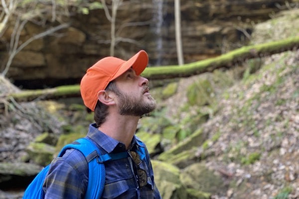 Hiker out in the woods wearing a bright orange baseball cap