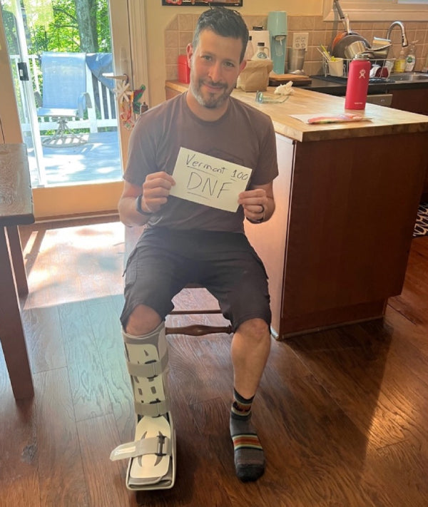 Jared with his foot in boot holding a Vermont 100 DNF sign