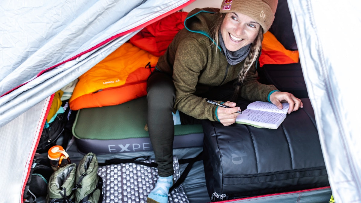 Professional Skier Michelle Parker smiling out of her tent in the Tordrillo Mountains, writing in her notebook