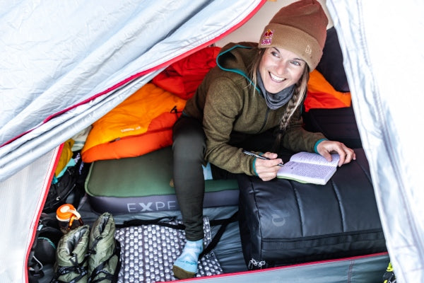 Michelle Parker in a tent surrounded by snow writing in a journal with her Darn Tough Ski socks on
