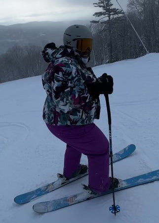 Mirna on top of a ski slope, smiling back before she heads down