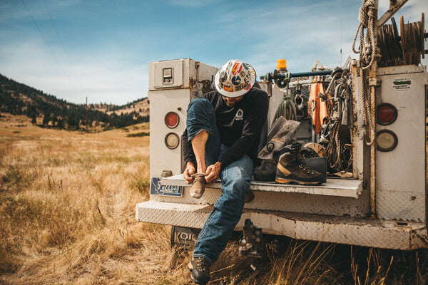 Telephone lineman seated on back of track pulling on boots and wool fire resistant socks