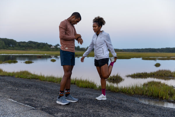 Two people stretching before a run in Darn Tough running socks