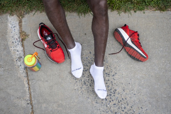 Runner seated on ground wearing white socks putting on training sneakers