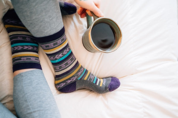 Woman seated on bed drinking coffee in darn tough lifestyle casual socks