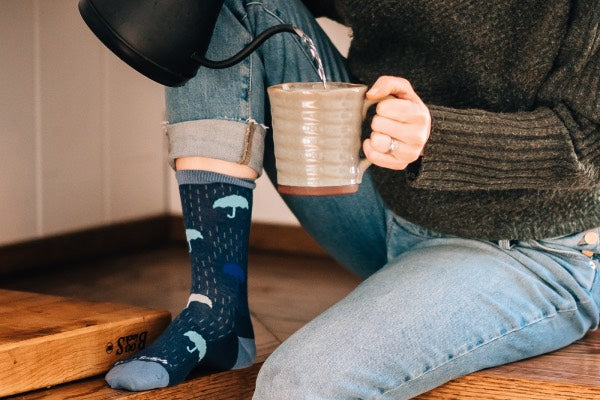 Woman seated on counter pouring tea while wearing the umbrella everyday socks