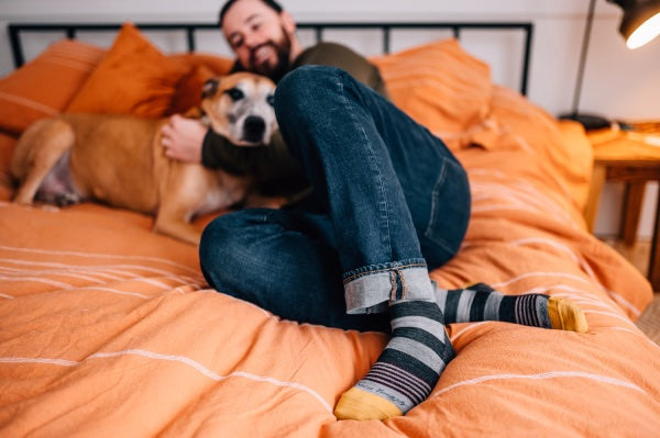 Man on bed hugging dog while wearing striped lifestyle socks
