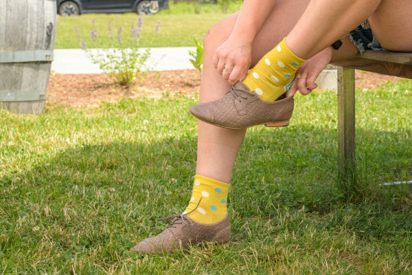 Feet wearing yellow socks with polka dots from darn tough, putting on booties
