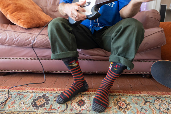 Person seated on couch playing air guitar wearing lifestyle socks with a guitar playing squirrel