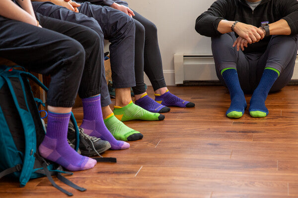 Four people seated around room, all wearing limited edition socks in bright colors like purple, green, and blue