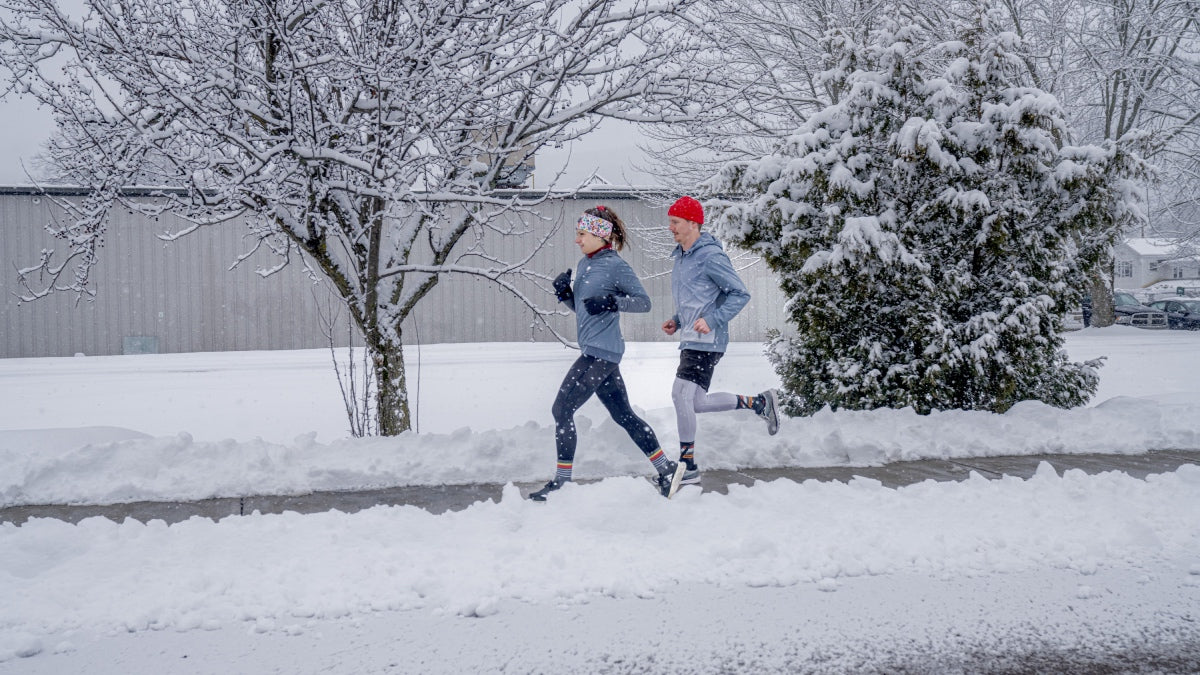 Two runners outside running in the winter, with snow falling around them