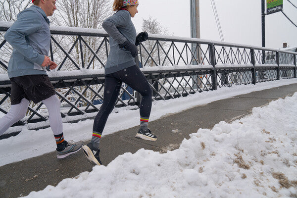Two people running across a bridge surrounded by snow on a winter day