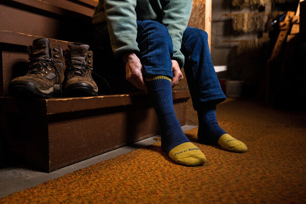 Feet pulling on merino wool work socks in blue and yellow