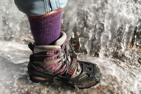 Closeup on foot wearing hiking boots, darn tough socks, and micro spikes, standing on ice