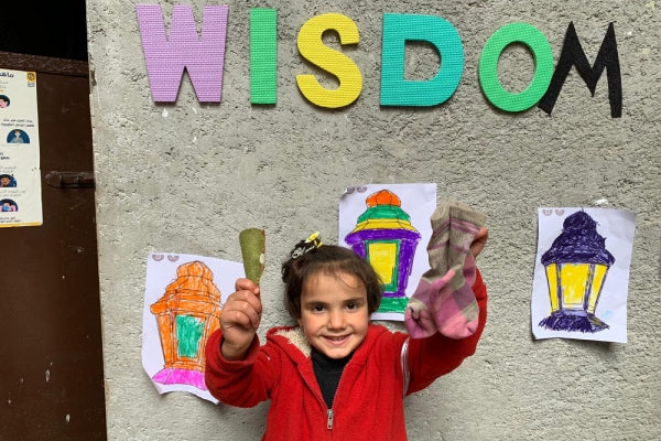 A little girl smiling under the Wisdom House sign, holding a pair of socks