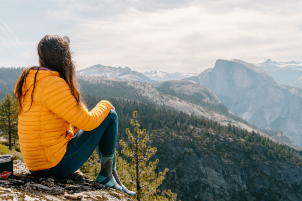 Woman sitting on a mountain top looking at the mountains in Darn Tough socks