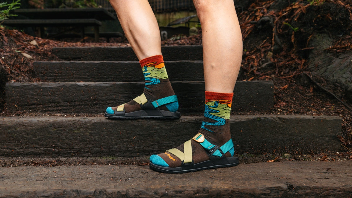 Feet standing on steps wearing Darn Tough hiking socks and sandals that show them off