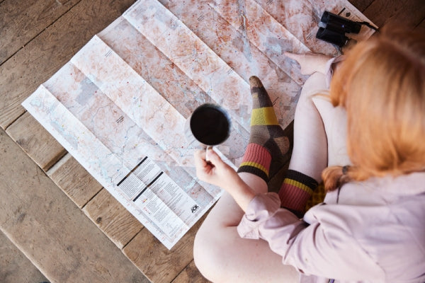 Woman reading a map, drinking from a mug, and wearing Darn Tough Socks