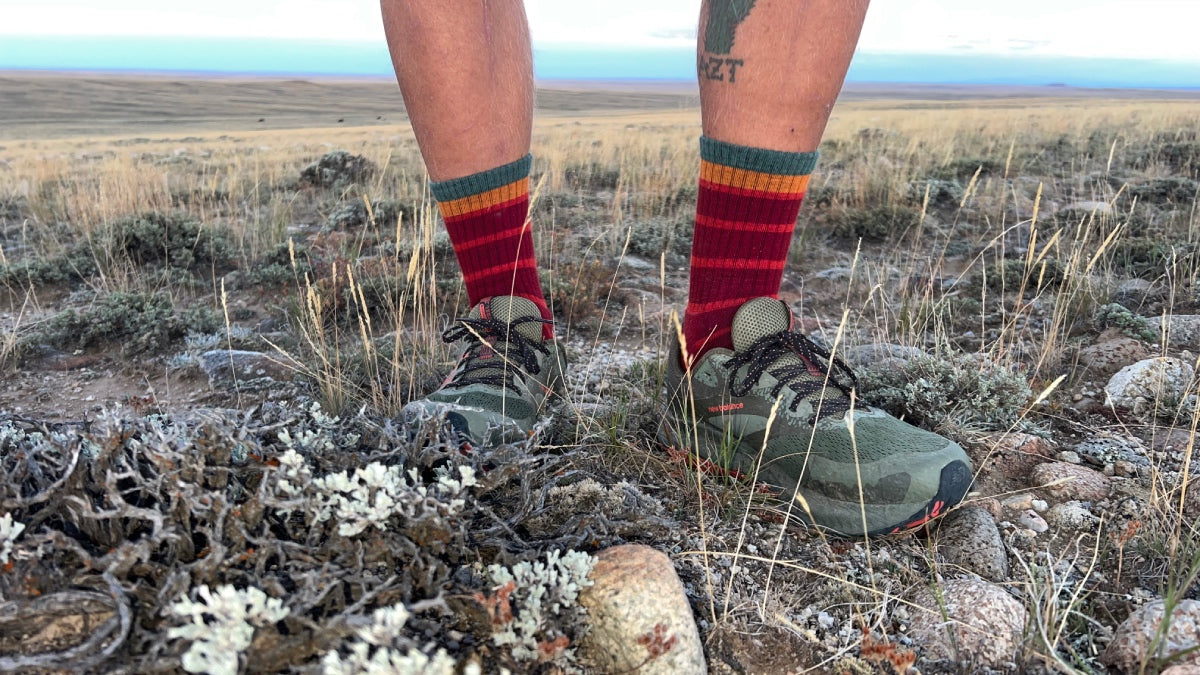 A pair of feet on the CDT wearing red Darn Tough hiking socks with stripes