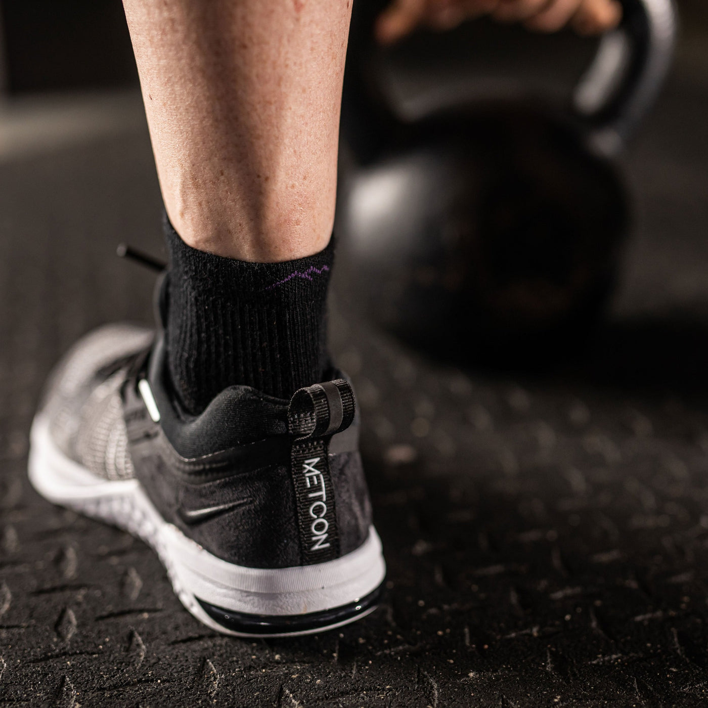 Close up image of a woman's feet, with a kettlebell in the background, wearing a sneaker and Women's Element Quarter Lightweight Athletic Socks in Black, Lifestyle Image