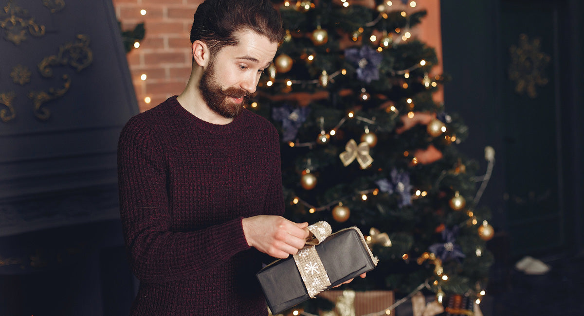 Man Opening Gift in front of a Christmas Tree
