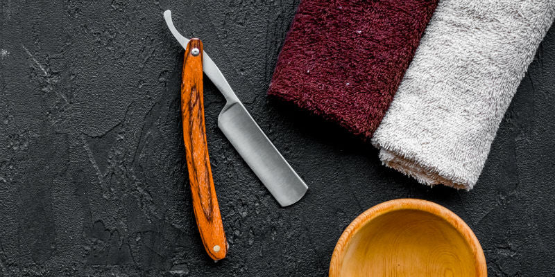 top-down view of cut-throat razor, towel, and bowl, on slate surface